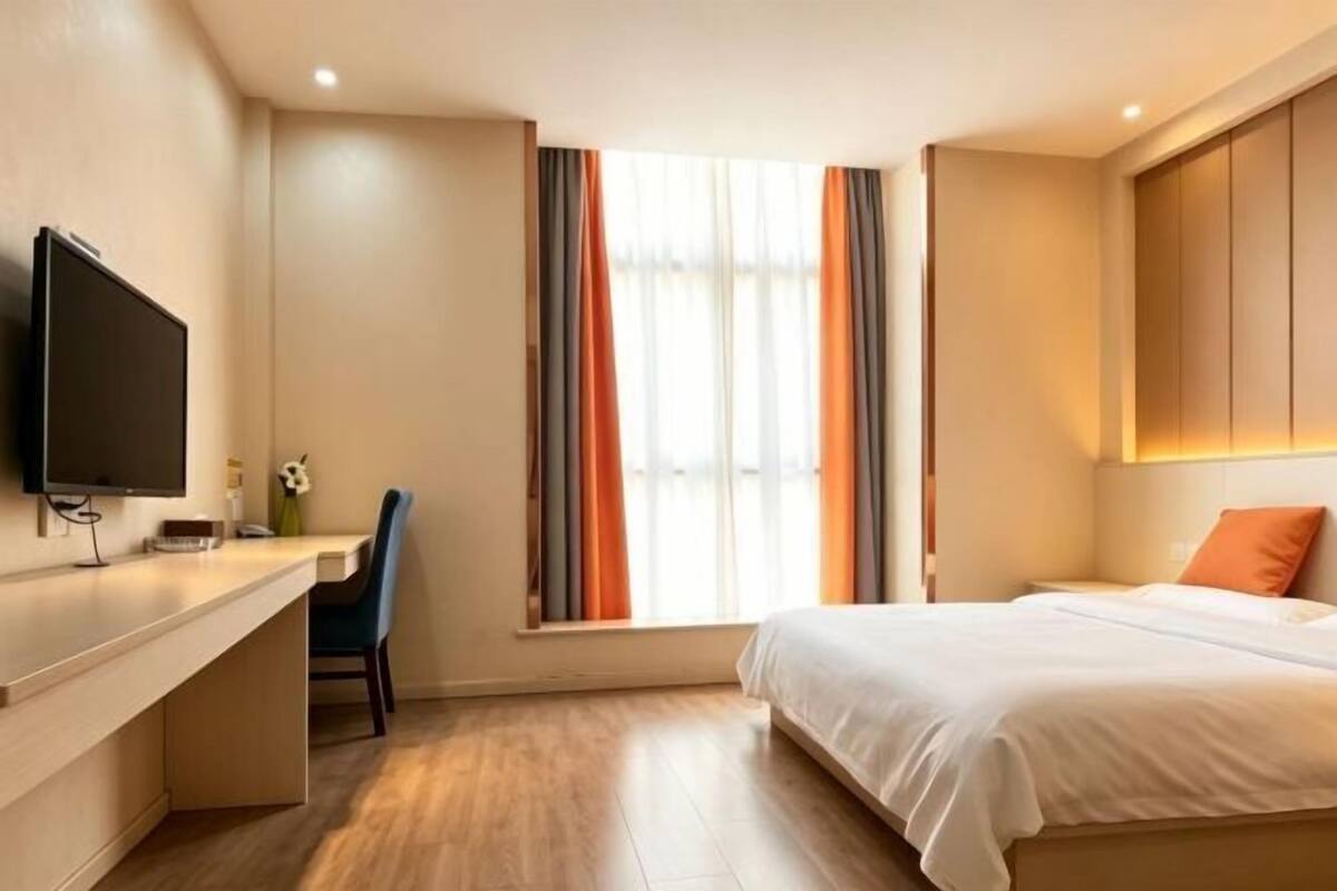A hotel room with a bed, a desk, a chair, a television, and a window with curtains.