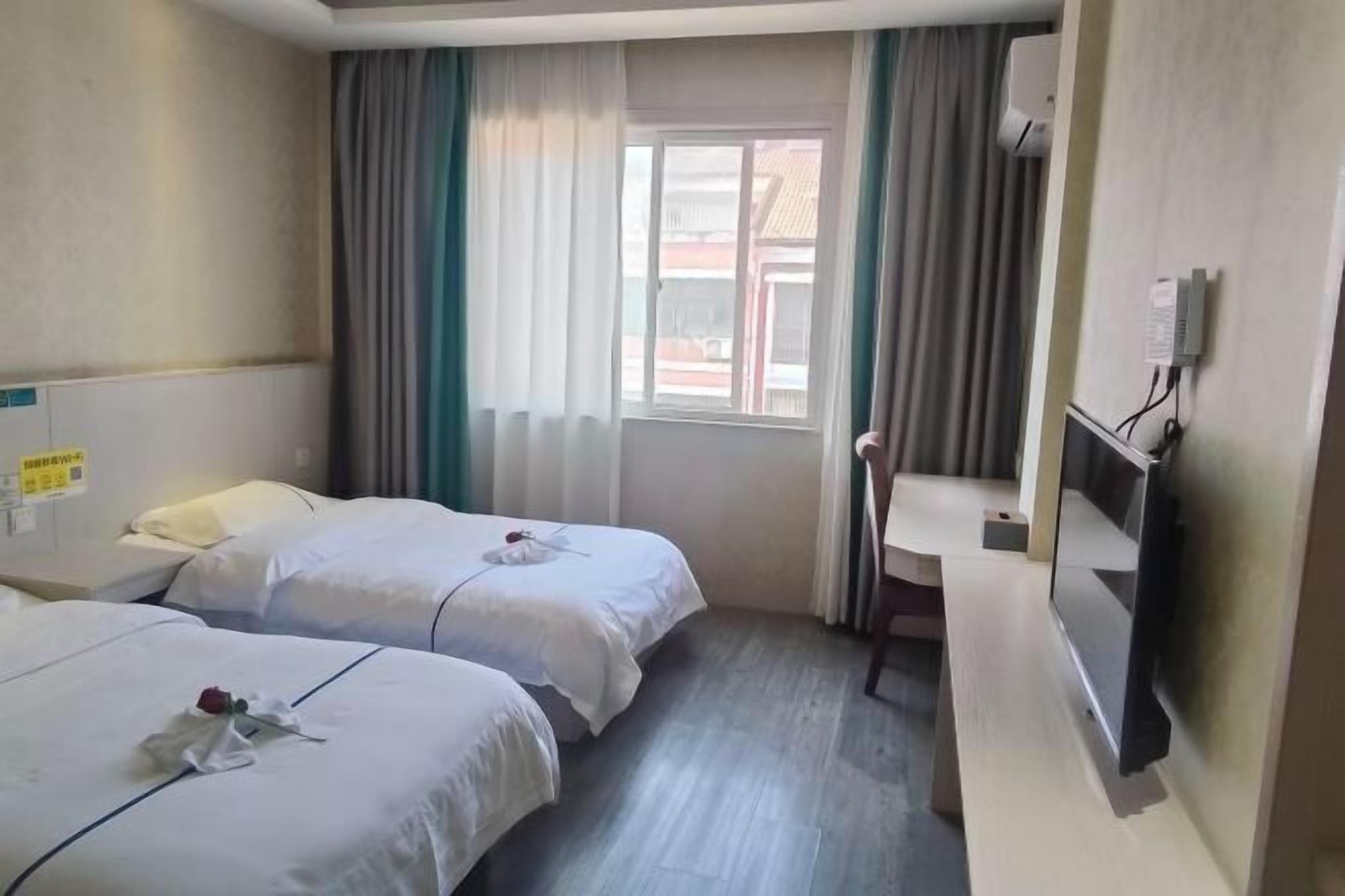 Ein Hotelzimmer mit zwei Betten, einem Schreibtisch, einem Fernseher und einem Fenster mit Vorhängen.