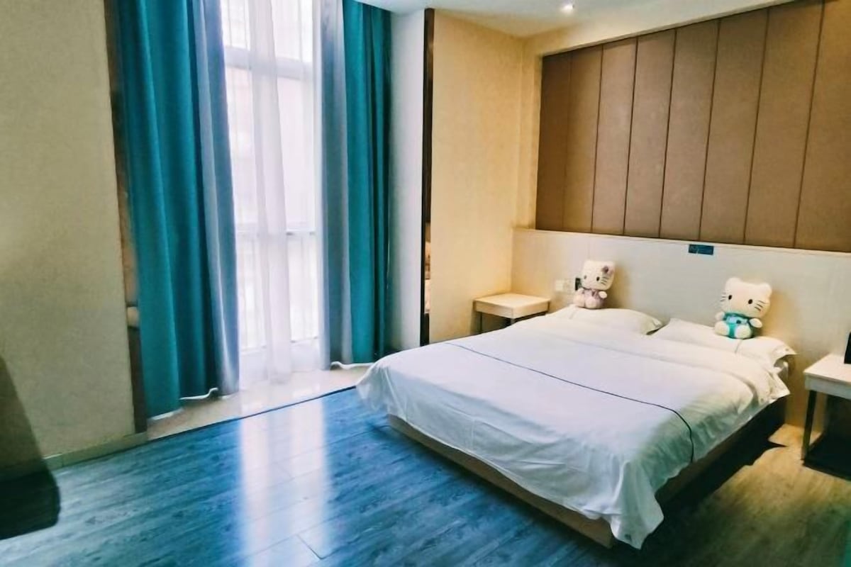 Una habitación de hotel con una cama grande, una mesita de noche, una ventana con cortinas y un cabecero.