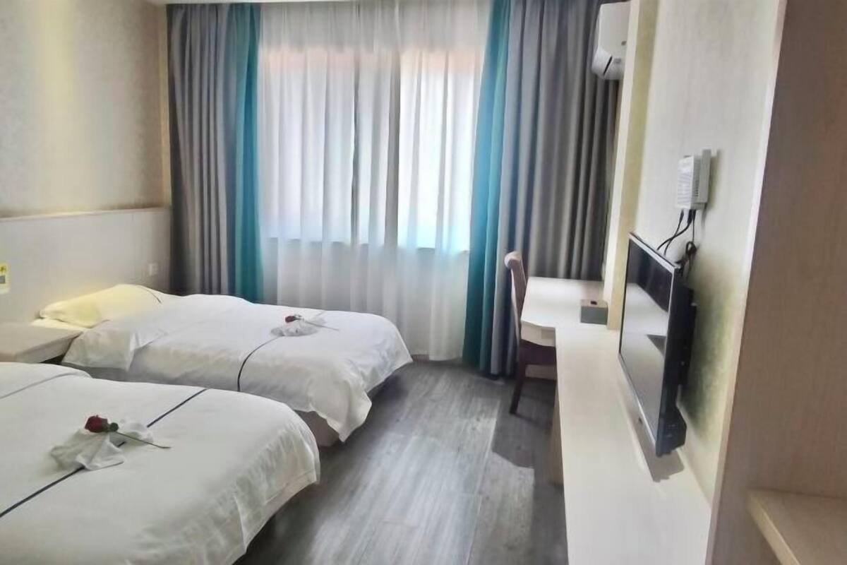 A hotel room with two beds, a desk, a chair, a TV, and a window with curtains.