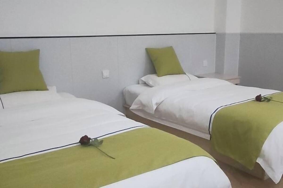 Two single beds with green and white bedding, a white wall, and a small bedside table.
