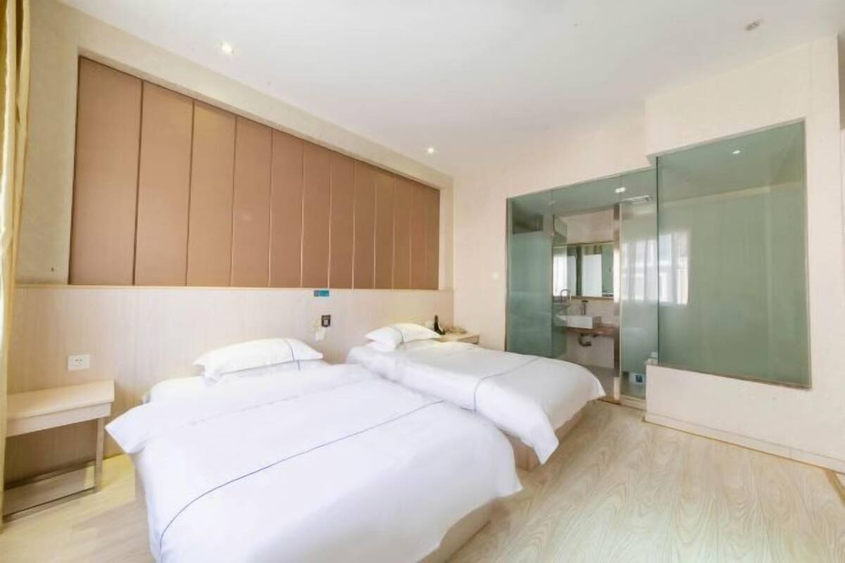 A hotel room with two beds, a large mirror, and a glass partition wall.