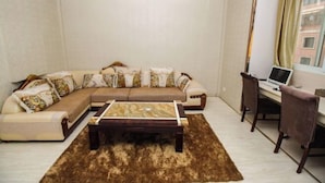 A living room with a sectional sofa, a coffee table, a desk with a laptop, and a chair. - Xuancheng Guangde Wanjia Express Inn (Guangde)