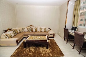 A living room with a sectional sofa, a coffee table, a desk with a laptop, and a chair. - Xuancheng Guangde Wanjia Express Inn (Guangde)
