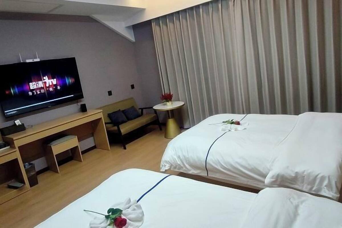 A hotel room with two beds, a TV, a small table with a vase, and a sofa.