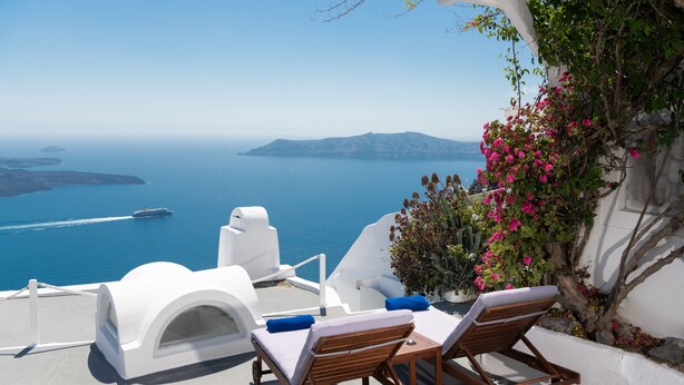 A seaside terrace with white architecture, two wooden lounge chairs, a small table, and a view of the sea and islands. - Impeccable Double Bed Villa in Imerovigli Santorin (Santorini)