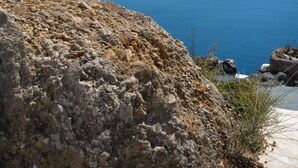 A rocky terrain with a clear view of a large body of water and distant landforms. - Impeccable Double Bed Villa in Imerovigli Santorin (Santorini)