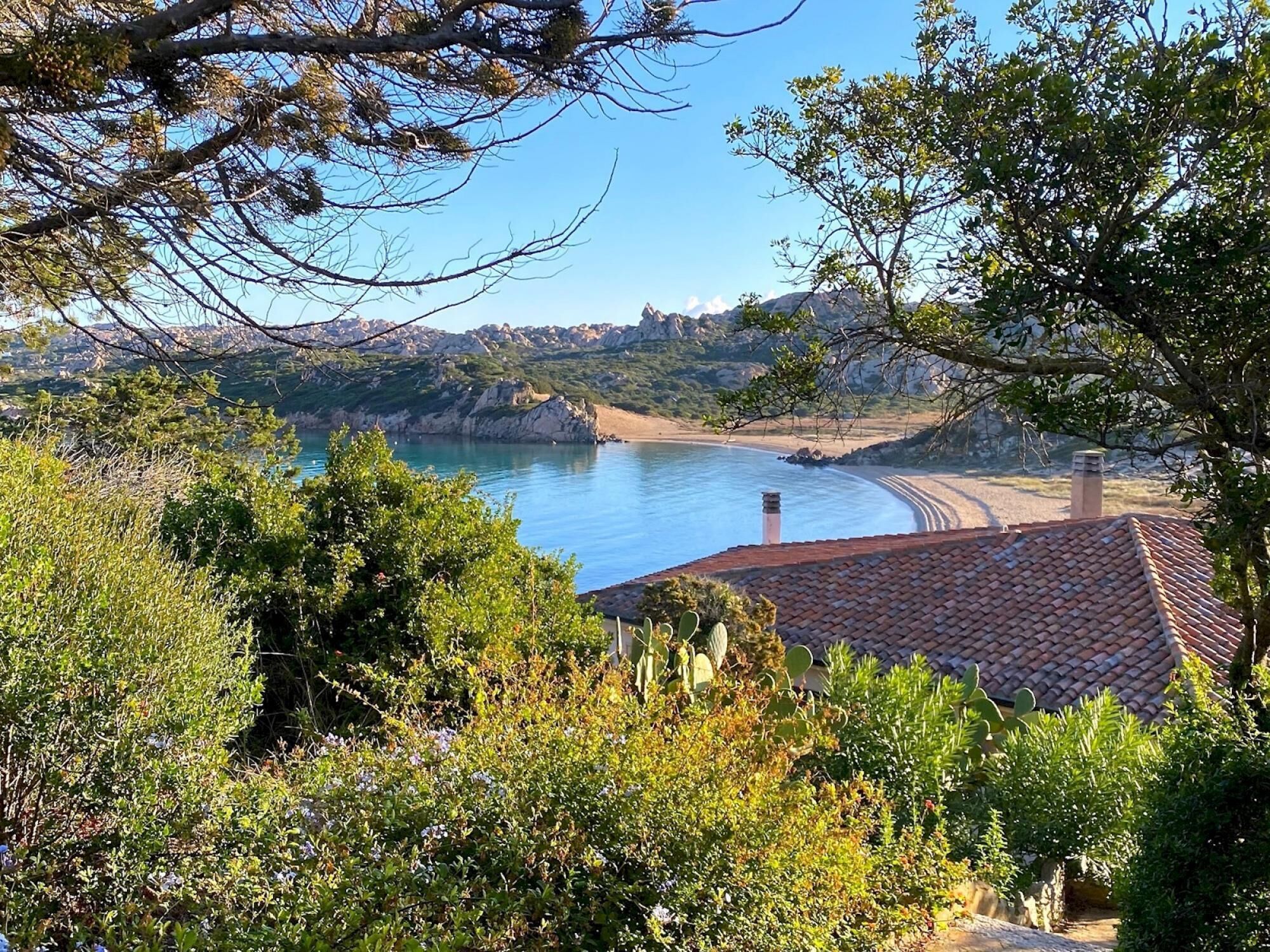 A coastal view with a beach, rocky cliffs, and a house with a tiled roof.