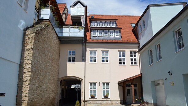 Un edificio europeo tradicional con fachada de piedra, múltiples ventanas y techo de tejas rojas.