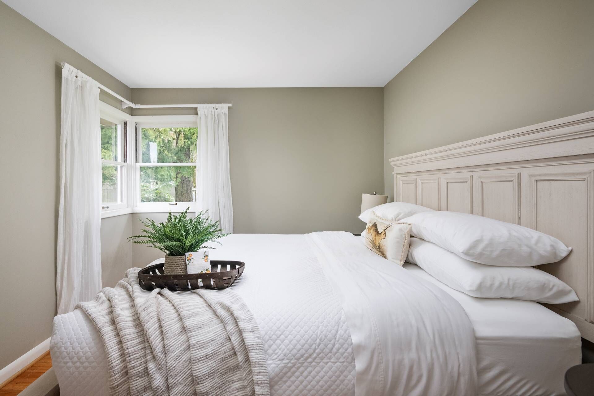 Une chambre à coucher avec un lit, une fenêtre avec des rideaux, une table de chevet avec une plante et une lampe.