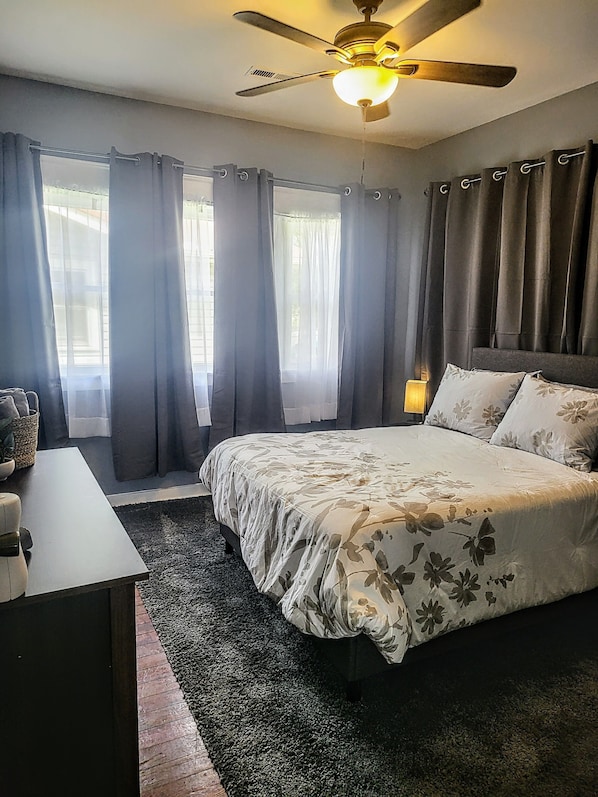 A bedroom with a bed, a desk, a lamp, and a ceiling fan.