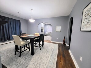 A dining area with a table and chairs, a rug, and a painting on the wall.