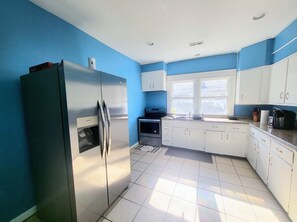 A kitchen with white cabinets, a stainless steel refrigerator, a window, and a tiled floor.