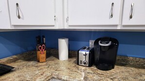 A kitchen with white cabinets, a granite countertop, a toaster, a coffee maker, and a paper towel holder with scissors. - Bright & Cozy, near downtown & hiking trails (Birmingham)
