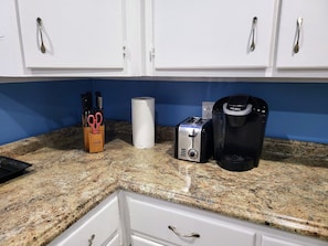 A kitchen with white cabinets, a granite countertop, a toaster, a coffee maker, and a paper towel holder with scissors.