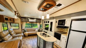 A compact RV interior with a kitchenette, a dining area, and a seating area with a view of the outdoors.