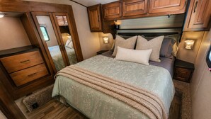 A bedroom with a bed, wooden cabinets, a dresser, and a window.
