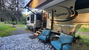 An RV with a covered porch area, outdoor seating, and a staircase leading to the entrance.