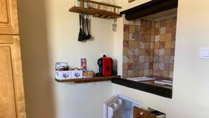 A compact kitchen with a wooden shelf holding kitchen utensils, a coffee maker, and a small refrigerator. - Appartamento Volta Della Vecchia (Florence)