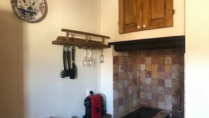 A kitchen with a tiled backsplash, a wooden cabinet, a shelf with kitchen utensils, and a coffee maker. - Appartamento Volta Della Vecchia (Florence)