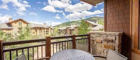 A balcony with a round table and chairs, overlooking a mountainous landscape with multiple buildings.