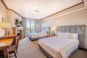 A hotel room with two beds, a desk, a chair, a fireplace, and a view of the outdoors.