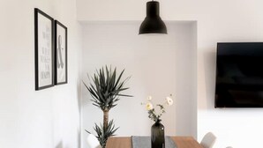 Ein moderner Essbereich mit einem Holztisch, weißen Stühlen, einer schwarzen Pendelleuchte, einer Topfpflanze und einer Vase mit Blumen.