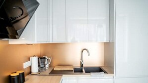 Eine moderne Küche mit weißen Schränken, einer Edelstahlspüle, einer Kaffeemaschine und einem Wasserkocher.