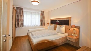 A bedroom with a wooden bed, two bedside tables, a nightstand, a wall-mounted TV, and a window with curtains. - Ferienwohnung Gederer für 2-5 Personen (Bernau am Chiemsee)