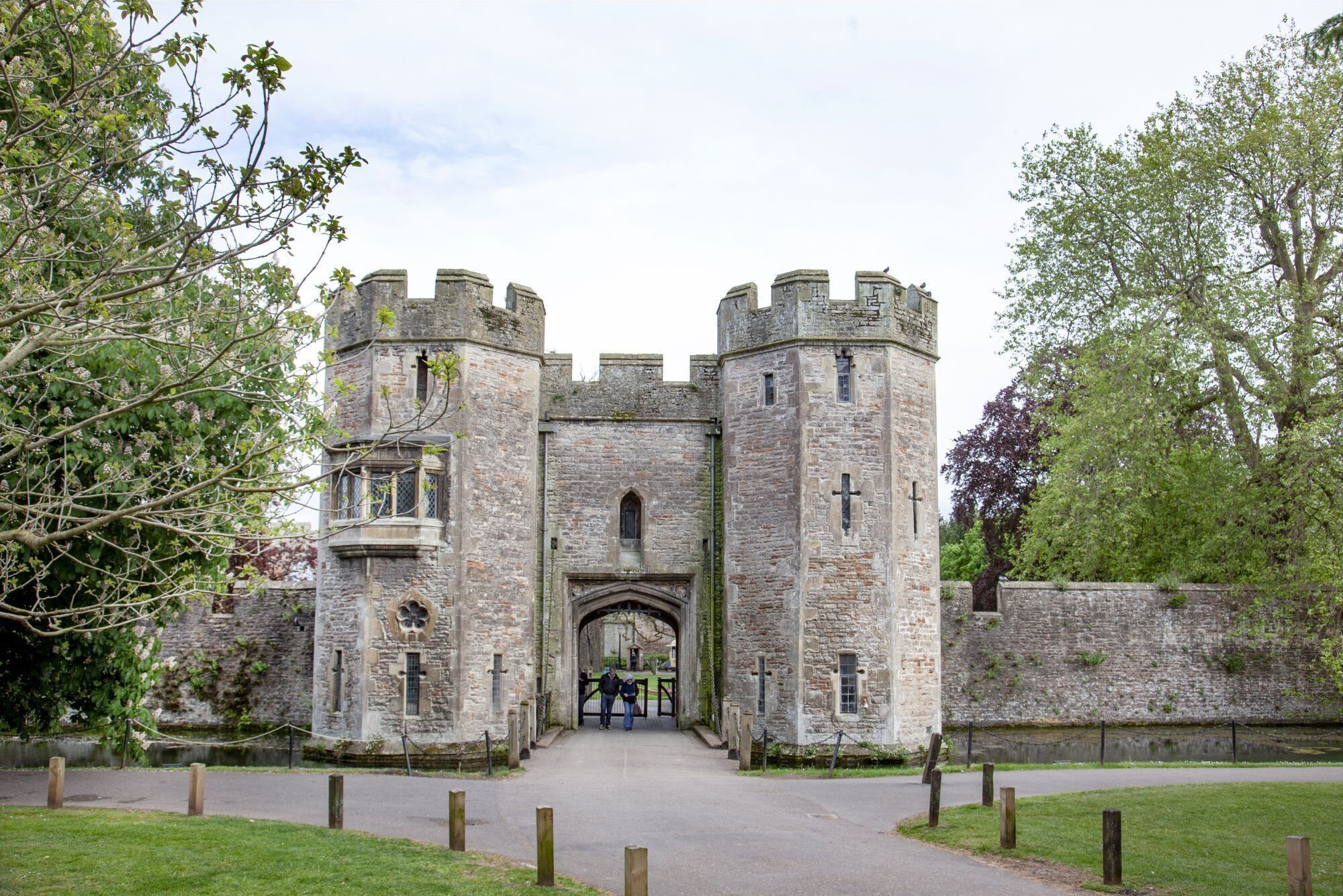 A historic stone castle with a central archway and two towers, surrounded by a grassy area and trees.