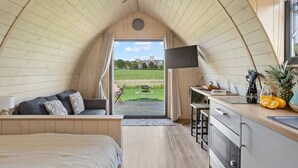 Um quarto aconchegante, tipo tenda, com cama, área de estar, cozinha compacta e uma grande janela com vista para um campo verde e um edifício ao longe.