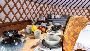 A dining area with a table set for two, featuring a teapot, bowls, plates, and utensils. - Kestrel Yurt, with hot tub, Hawes, Yorkshire Dales (Askrigg)