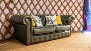A green leather sofa with tufted detailing and decorative pillows against a lattice backdrop. - Kestrel Yurt, with hot tub, Hawes, Yorkshire Dales (Askrigg)
