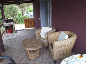 Uma área de varanda coberta com móveis de vime, uma pequena mesa e um balde vermelho.