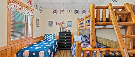 A room with two beds, a wooden bunk bed, a window with blinds, and baseball-themed decor.