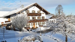 Eine zweistöckige Chalet mit Balkon, umgeben von schneebedeckten Bäumen und einem klaren Himmel.