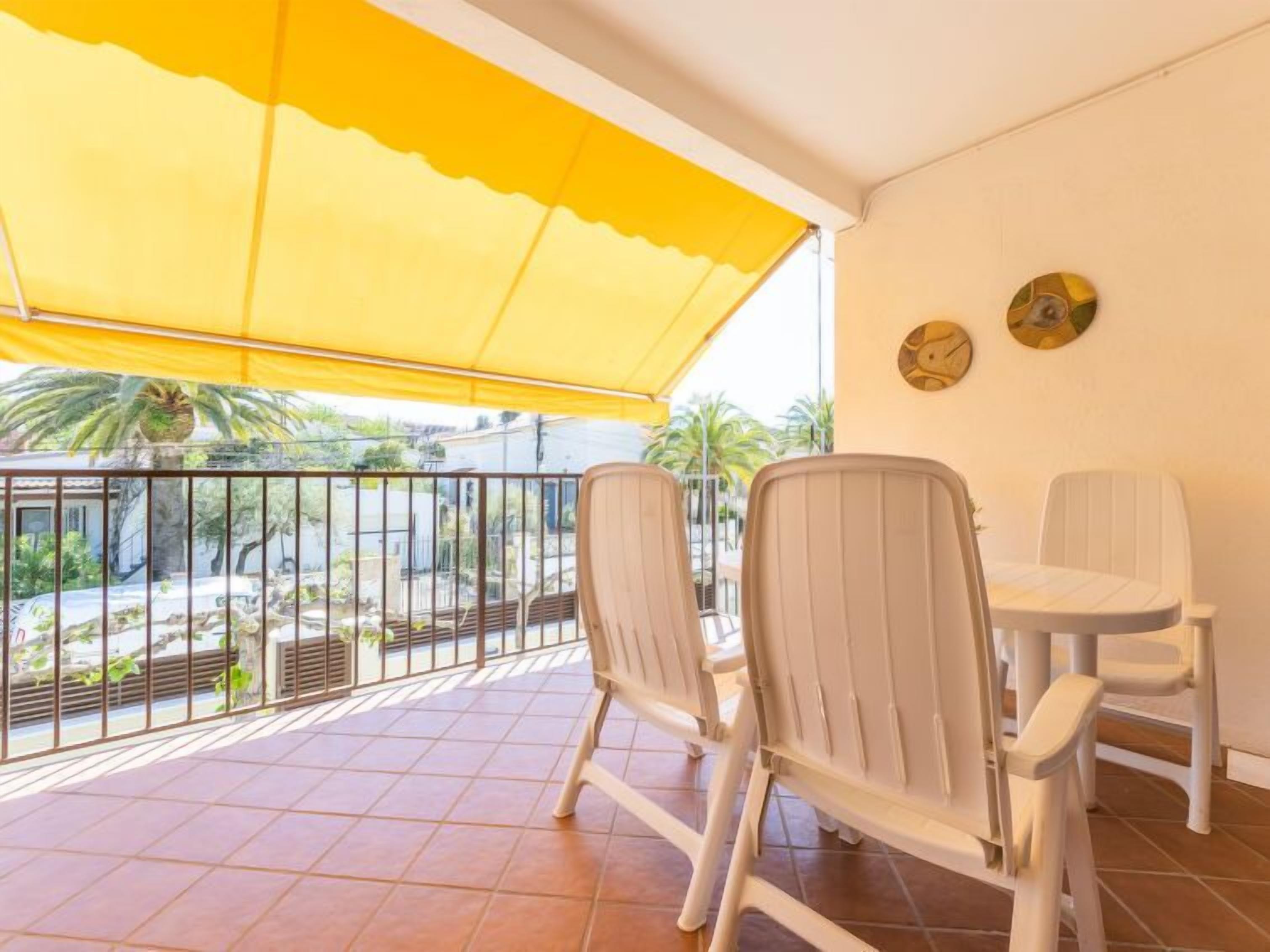 Ein Balkon mit gelbem Markisenstoff, weißen Stühlen und gefliestem Boden.