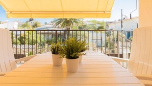 En balkon med gul markise, hvide stole og to krukker med planter.
