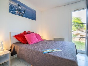 Een slaapkamer met een bed, kussens, een nachtkastje, een raam en een schilderij aan de muur.