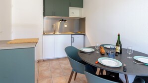 Une cuisine compacte comprenant un coin repas, un réfrigérateur et une table dressée pour deux personnes, avec des assiettes, des verres et une bouteille.