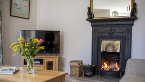 A living room with a fireplace, a television, a wooden table with a vase of flowers, and a wicker basket. - Brook House, Askrigg, Yorkshire Dales (Askrigg,)