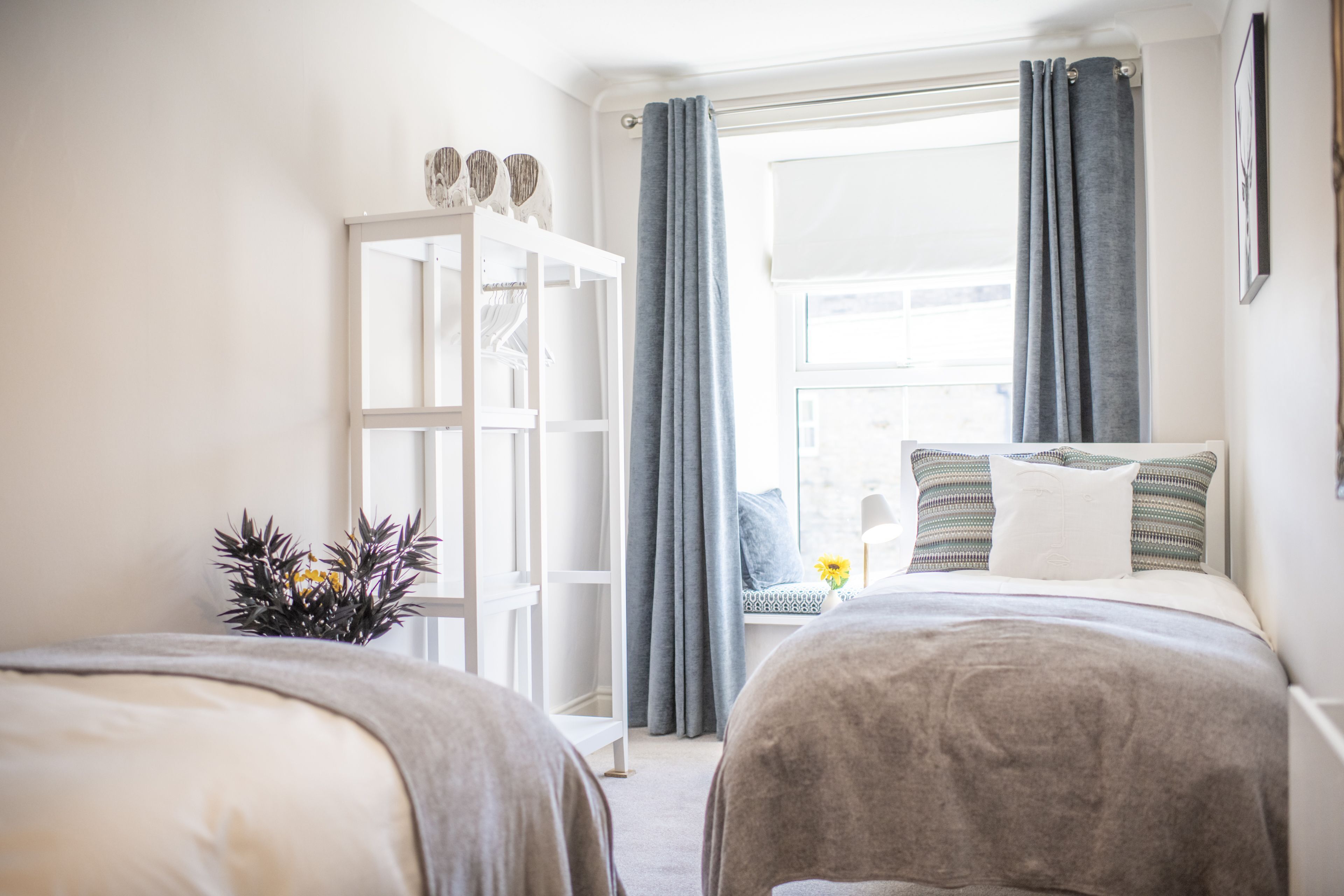 Quarto com duas camas, guarda-roupa, janela com cortinas e vista exterior.