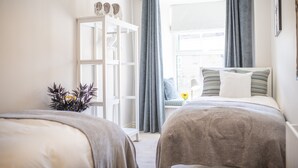 A bedroom with two beds, a wardrobe, a window with curtains, and a view of the outside. - Brook House, Askrigg, Yorkshire Dales (Askrigg,)