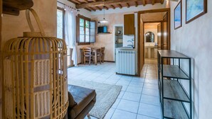 Ein gemütliches Zimmer mit Holzbalkendecke, einer Essecke mit Tisch und Stühlen, einer Küche mit Spüle und Schränken sowie einem großen Fenster mit Vorhängen.