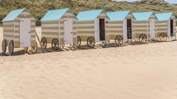 A row of beach huts with striped walls and blue roofs, each with a door and a wheel attached to the front. - Klemskerkestraat with terrace by Interhome (Bredene)