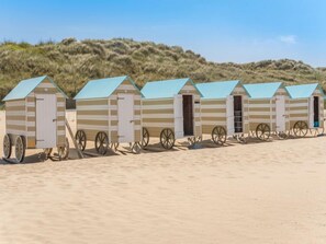 A row of beach huts with striped walls and blue roofs, each with a door and a wheel attached to the front. - Klemskerkestraat with terrace by Interhome (Bredene)