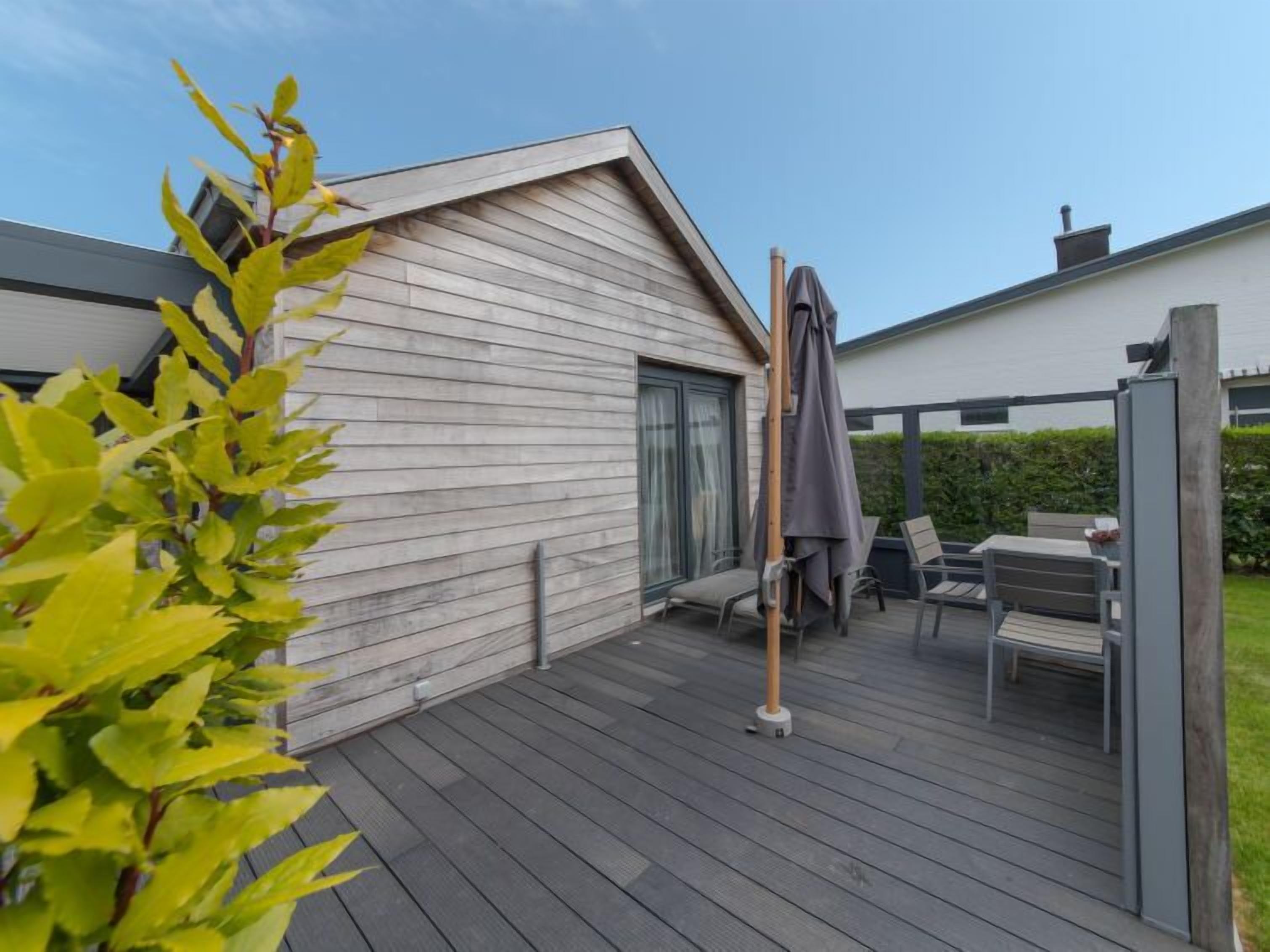 Une terrasse dotée de mobilier d’extérieur, d’une pergola et offrant une vue sur une maison moderne.