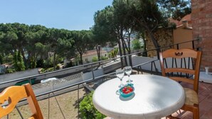 A round table with two chairs on a balcony, a bowl of fruit, and two glasses.