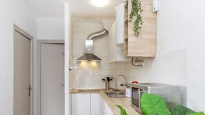A compact kitchen with white cabinetry, a stainless steel range hood, a built-in microwave, and a sink.