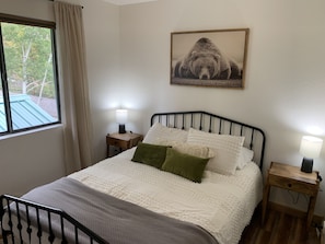 A bedroom with a bed, two bedside lamps, a window with a view, and a framed picture on the wall.